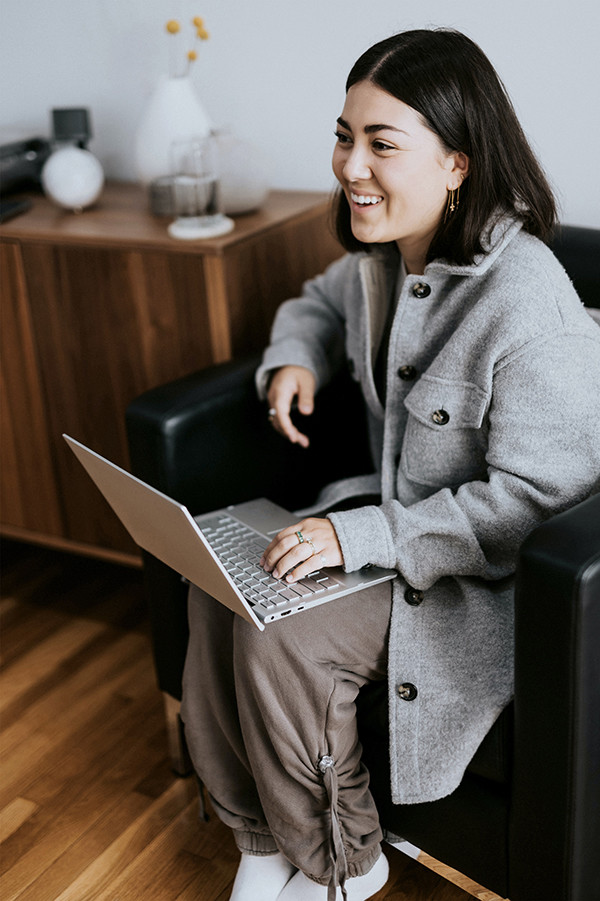 Mujer sonriente y amigable hablando con una computadora portátil en su regazo en un sillón